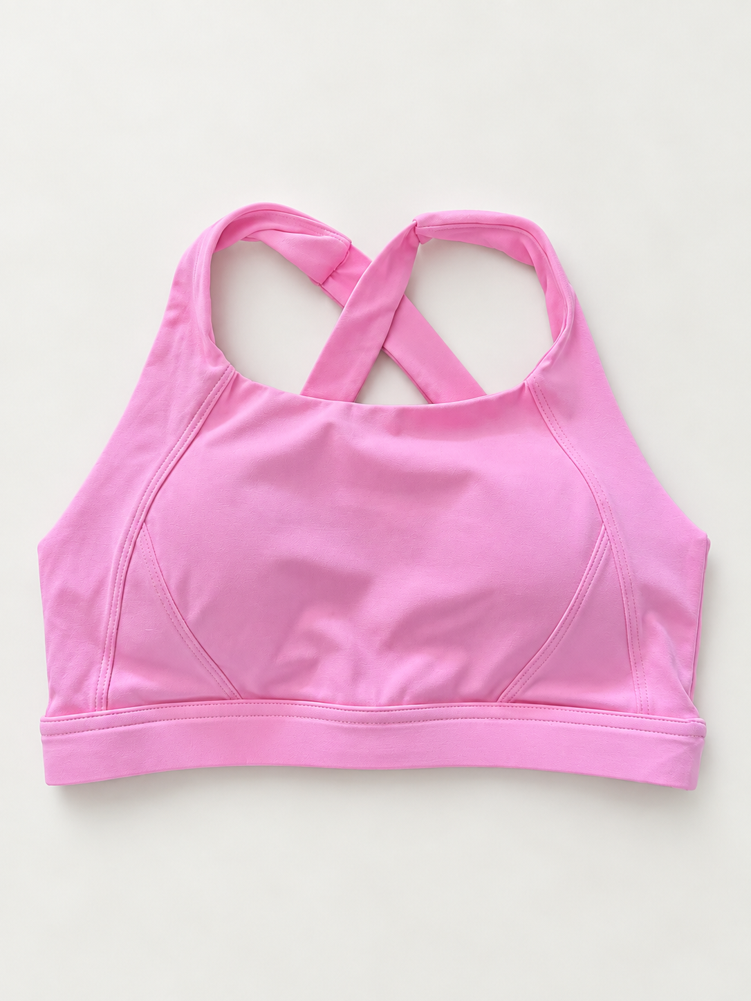 A pink sports bra with a crossover crisscross back strap design, laid flat on a light off-white background.